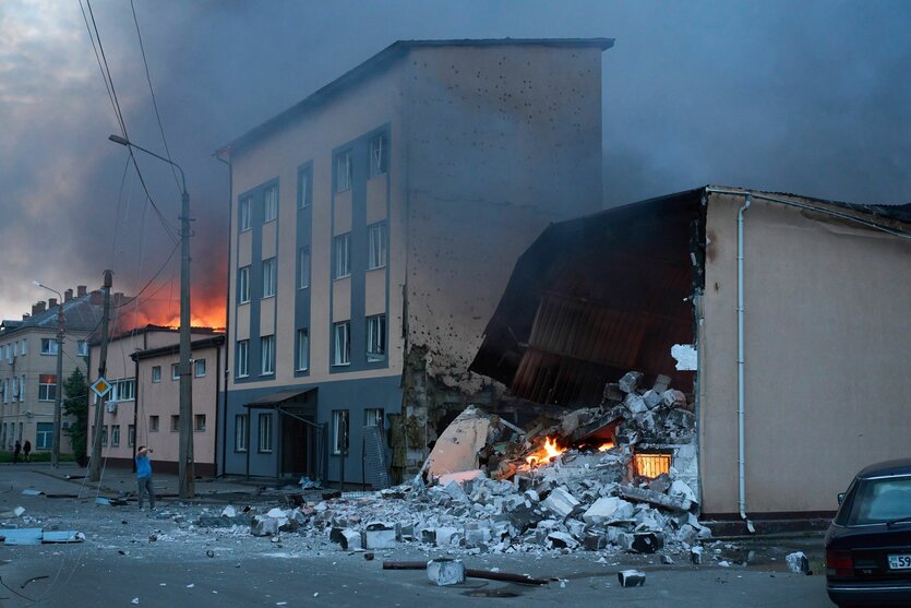 Ein halb zerstörtes Haus, dahinter steigt schwarzer Rauch auf