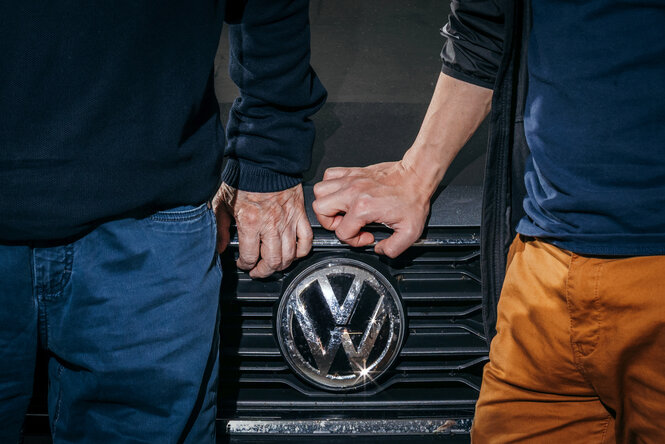 Zwei Personen im Ausschnitt stehen vor einem VW-Zeichen.