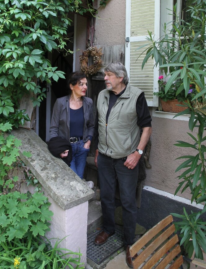 Ein Mann und eine Frau stehen nebeneinander vor einem Haus mit Garten