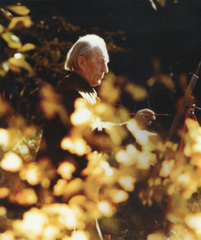 Ein Mann malt an einer Staffelei in einem herbstlichen Garten ein Bild