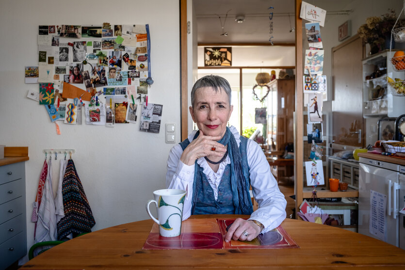 Judy Rosenthal sitzt in ihrer Küche, den Kopf leicht auf den Arm gestützt, mutig in die Kamera blickend