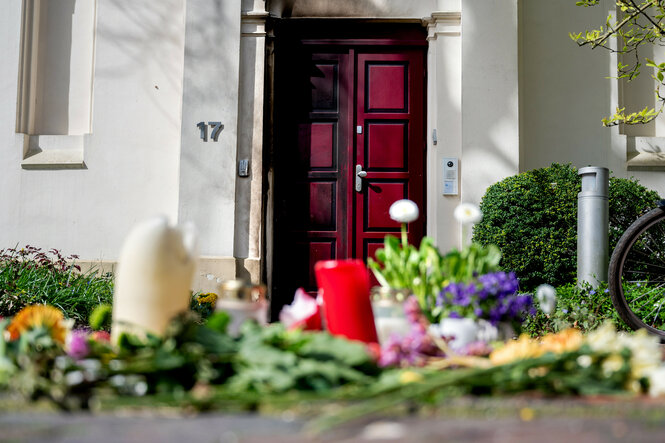 Blumen liegen vor einer Eingangstür, auf der Brandspuren zu sehen sind