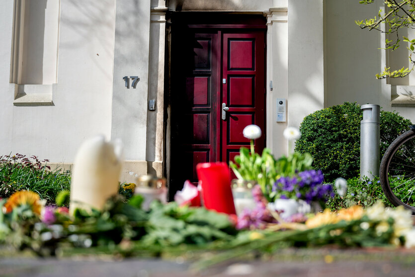 Blumen liegen vor einer Eingangstür, auf der Brandspuren zu sehen sind