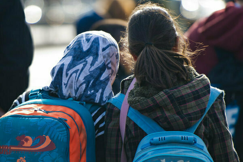 Mädchen mit Kopftuch und Schulranzen steht neben Mädchen ohne Kopftuch