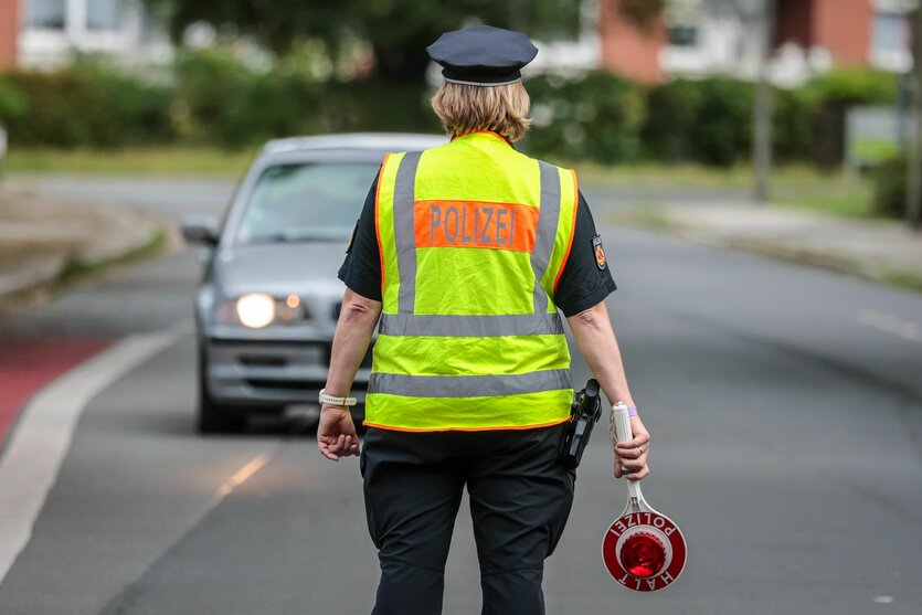 Eine Polizistin in gelber Warnweste steht in Bremen auf einer Straße, um den Verkehr zu regeln. In der Hand hält sie eine Kelle mit der Aufschrift "Halt Polizei".