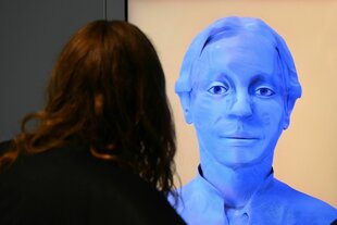 Ein KI-generierter Avatar im Gespräch mit einer Person die wir von hinten sehen.