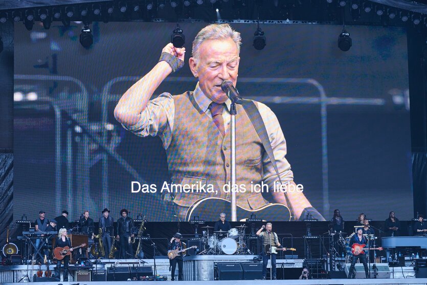 Bruce Springsteenauf der Bühne vor eine Leinwand, auf dem er selbst zu sehen ist. Und als eingeblendeter Untertitel: "Das Amerika, das ich liebe".