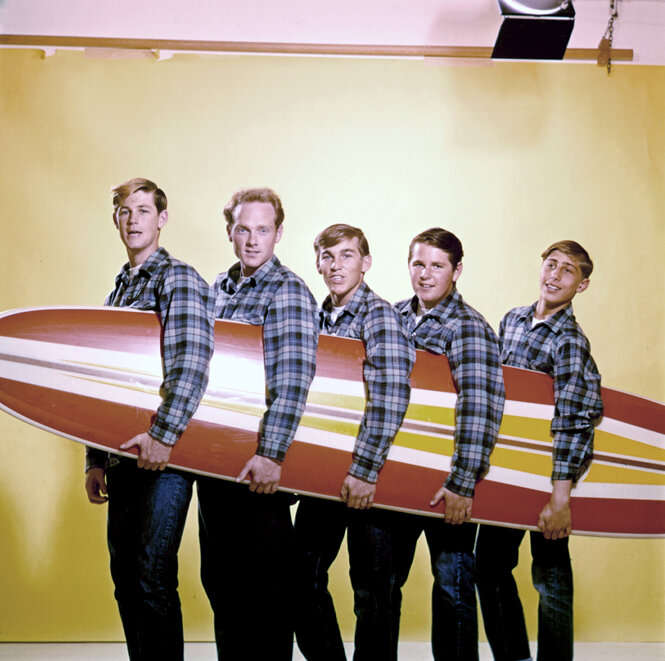 Die fünf Beach Boys halten zusammen ein Surfbrett