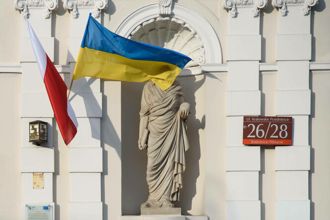 Mehrere Personen laufen an einem Haus vorbei, an dem eine polnische und eine ukrainische Falagge hängt.