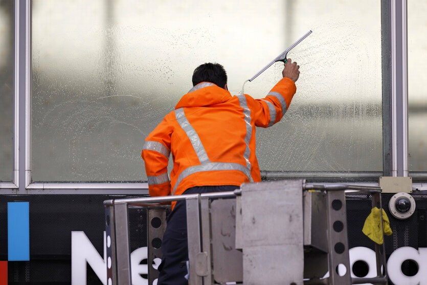 Ein Fensterputzer reinigt auf einer Hebebühne die Scheiben der Eingangshalle des Kölner Hauptbahnhofs