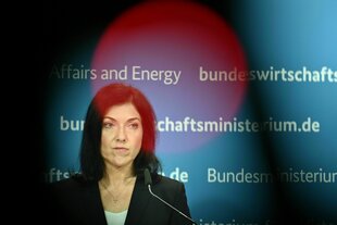 Katherina Reiche bei einer Pressekonferenz, sie verzieht die Mine und ein roter Schatten ist über ihrem Gesicht