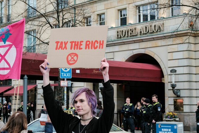 Demonstrant mit Schild "Tax the rich"