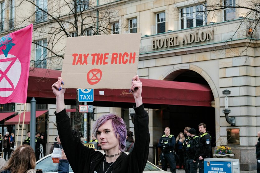 Demonstrant mit Schild "Tax the rich"