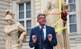 Mann im blauen Anzug vor einer alt aussehenden Gebäudefassade