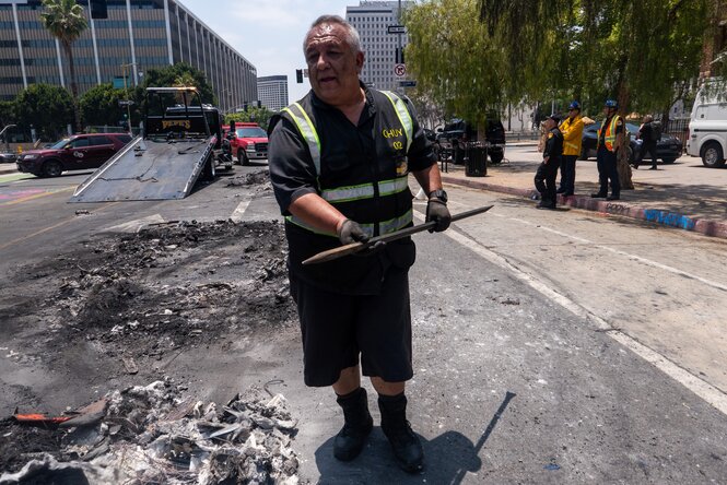 Ein Mann in Warnkleidung und mit Brechstange steht auf einer verrußten Straße