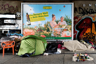 Ein Obdachlosenlager am Alex vor einem Werbeplakat 