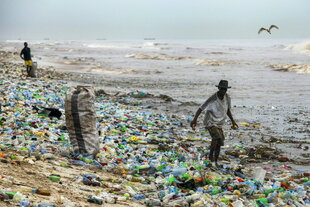 Menschen laufen über Plastikmüll am Strand