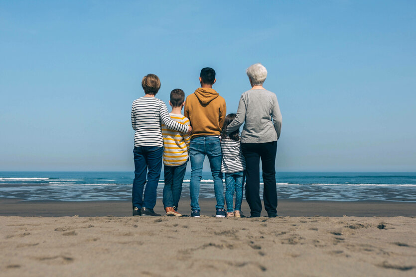 Fünf Personen stehen nebeneinander am Strand und schauen auf das Meer