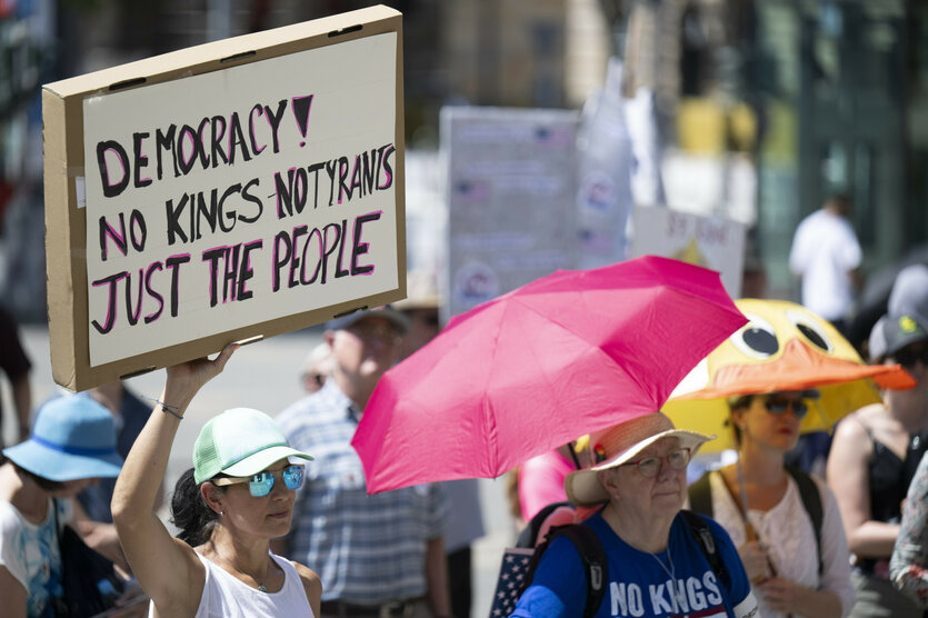 Eine Frau hält ein Schild in der Hand mit der Aufschrift "Democracy! No Kings - no Tyrants. Just the people"