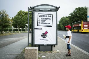 Ein Junge mit Basecap steht vor einem Werbeplakat