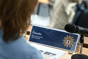 Ein von hinten fotografierter Kopf, auf dem Tisch vor der Person steht ein Schild mit dem Namen 