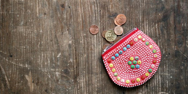 Eine bunte Geldbörse und Münzen liegen auf einem Holztisch