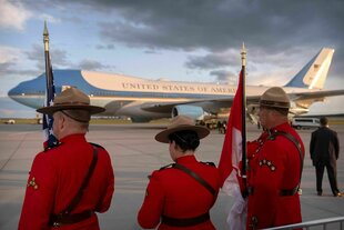 Drei rot-Uniformierte stehen vor der Air Force One auf einem Rollfeld