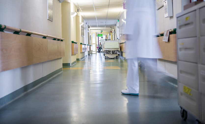 Eine Person im Kittel läuft einen leeren Krankenhausflur entlang.