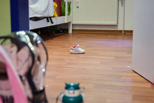 In einem Zimmer in einem Frauenhaus steht ein Kinderschuh, während der Schulranzen eines weiteren Kindes vor dem Zimmer steht