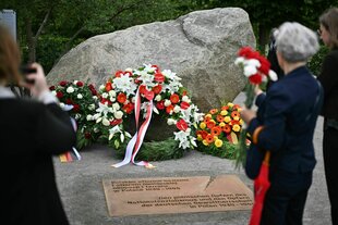 Menschen mit Blumen stehen während der Übergabe eines temporären Denkmals zur Erinnerung an die polnischen Opfer des Zweiten Weltkriegs und der deutschen Gewaltherrschaft vor dem dem Denkmal