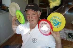 Ein älterer Mann mit schwarzem Basecap, weißem Shirt und mehreren bunten Frisbees