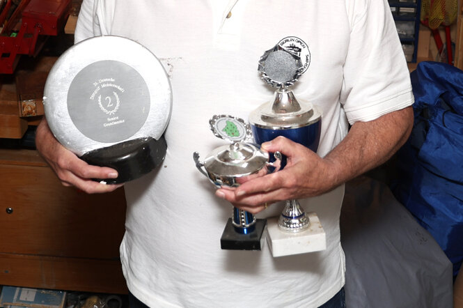 Eine Person trägt mehrere Pokal auf dem Arm.