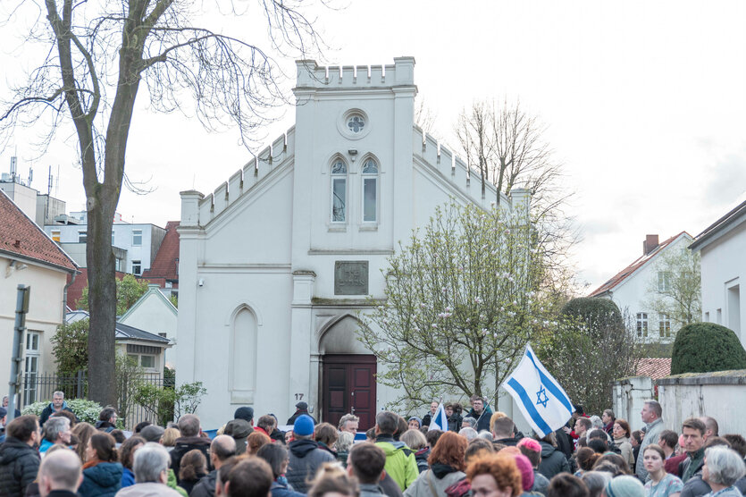 Eine Menschenmenge mit Israelfahne vor der Oldenburger Synagoge, deren Tür Brandspuren zeigt