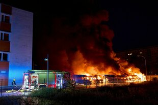 Flammen lodern nachts aus mehreren Lieferwagen, daneben ein Feuerwehrauto