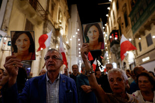 Menschen halten Fotos der verstorbenen Anti-Korruptions-Journalistin Daphne Caruana Galizia während eines Protestmarsches in der Nacht in die Höhe, sie haben die Flagge Malata mit sich