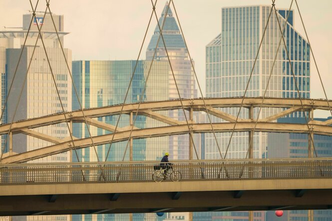 Ein Mann fährt mit seinem Fahrrad vor der Hochhauskulisse der Bankenstadt über die Osthafenbrücke