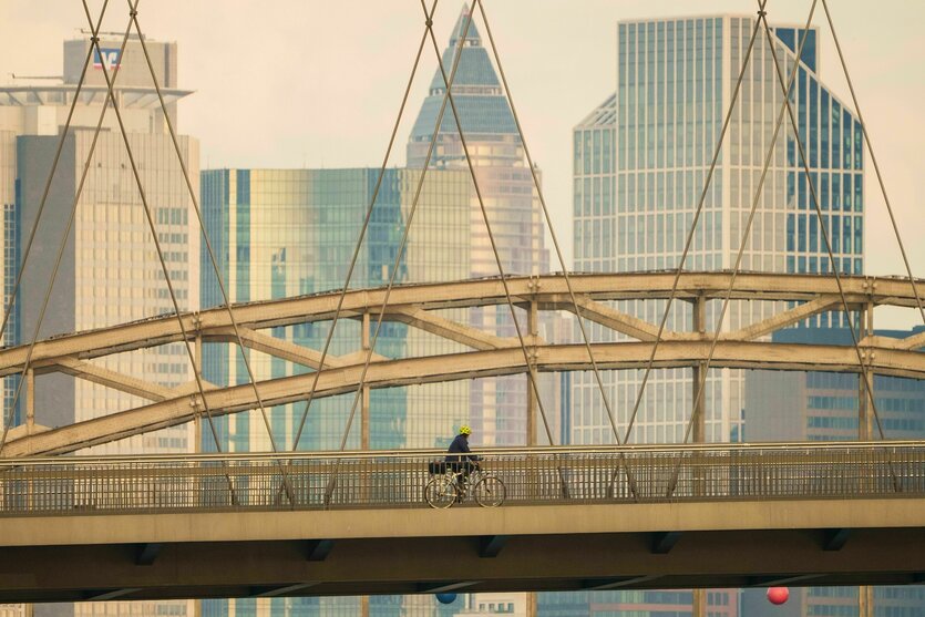 Ein Mann fährt mit seinem Fahrrad vor der Hochhauskulisse der Bankenstadt über die Osthafenbrücke