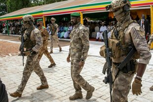 Eine Gruppe bewaffneter Männer umringt einen Mann, alle in der gleichen Uniform