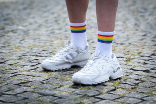 Detailaufnahme, Füße einer Person in weißen Turnschuhen und Socken, die Socken sind von der Regenbogen Flagge bekrönt