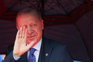 Der türkische Präsident Erdoğan steht unter einem Regenschirm und hält die Hand zum Gruß hoch