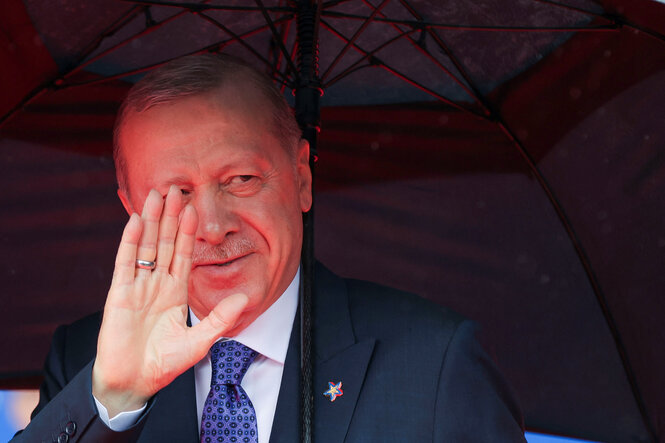 Der türkische Präsident Erdoğan steht unter einem Regenschirm und hält die Hand zum Gruß hoch