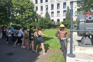 Der Künstler Toutou Ditchou zieht mit eine Gruppe von Zuschauern am Sockel eines Denkmals