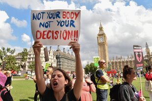 Eine Frau hält eine Plakt in die Höhe, im Hintergrund sieht man den Big Ben in London