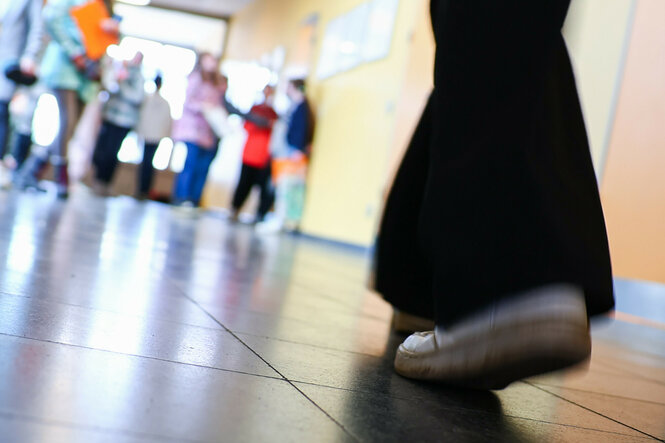 Ein Mädchen im bodenlangen Kleid und Turnschuhen geht durch einen Schulflur