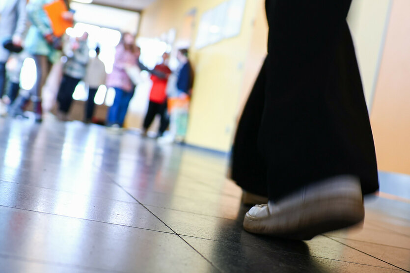 Ein Mädchen im bodenlangen Kleid und Turnschuhen geht durch einen Schulflur