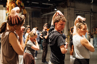 Drei Tänzer:innen greifen sich mit ihrer linken Hand über den Kopf ans rechte Ohr. Die Geste ist Teil der Choreographie gegen Trumps Zensur