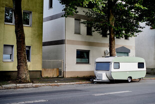 Ein Wohnwagen auf einer leeren Straße vor Wohnhäusern.