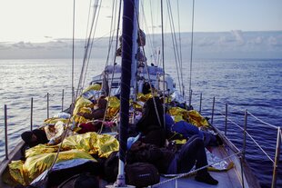Menschen, die in Schutzdecken gehüllt sind, liegen auf dem Deck eines Segelboots