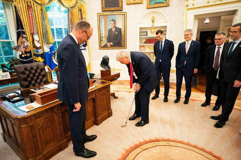 Trump hält einen Golfschläger in den Händen, er steht im Oval Offive und wird von anderen Personen umringt, einer von denen ist Friedrich Merz