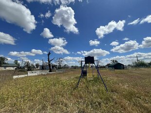 ein verdorrtes Feld mit einer verrosteten Schaukel, darüber blauer Himmel mit Wolken